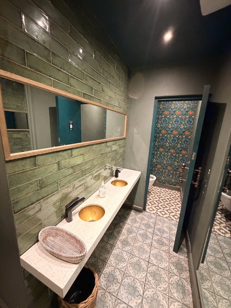 Women's restroom with sage green tiles and gold sinks